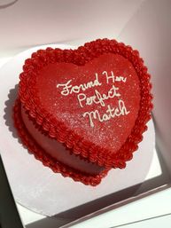 Heart-shaped red cake with ruffled icing border, sparkly red frosting and white piped message "Found Her Perfect Match" inside a white cake box