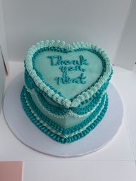 Heart-shaped teal cake with layered buttercream ruffles and piped "thank you next" message, sparkly finish on a white cake board