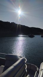 Glittering lake scene with bright sun and rainbow lens flare, sparkling water reflection, pontoon boat seating in the foreground and silhouetted hillside with distant boats