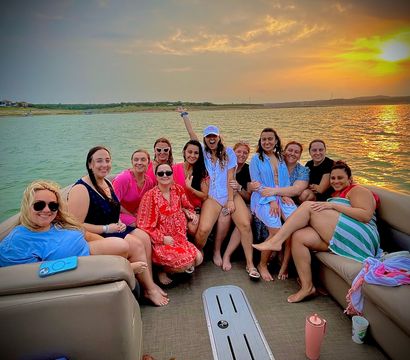 Group of friends on a pontoon boat at sunset on a lake, smiling women in colorful swimwear and cover-ups with the golden sun reflecting on the water