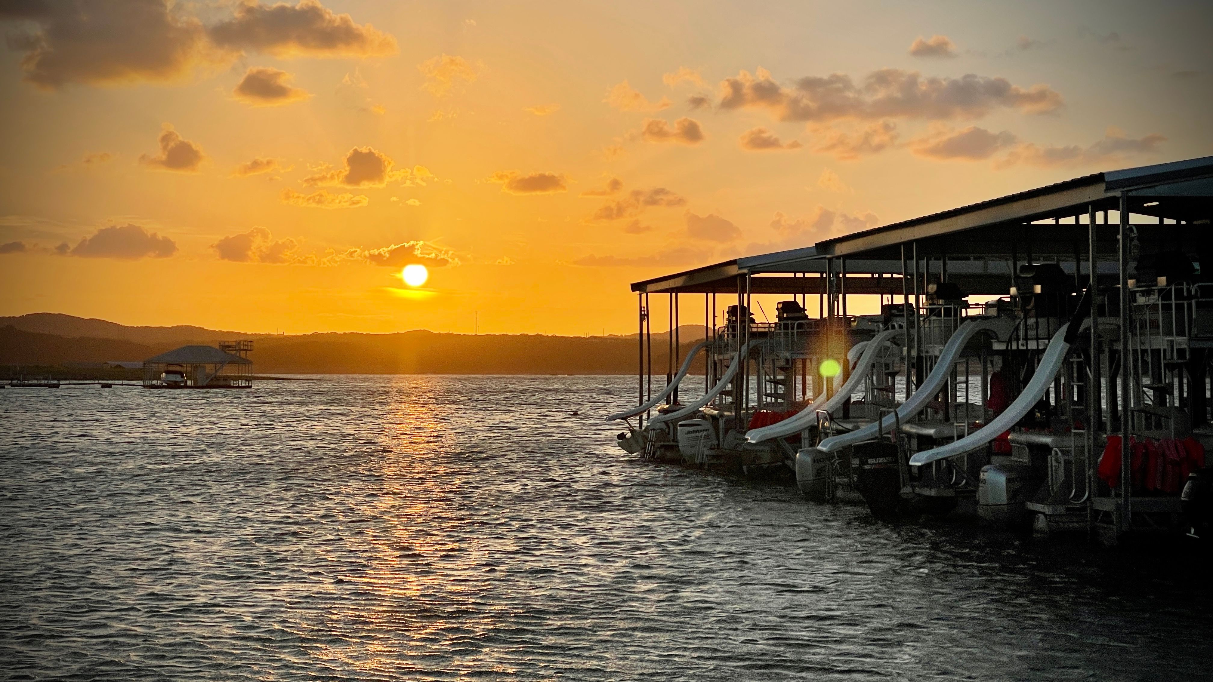 Golden sunset over a lake marina with docked boats and white water slides reflecting on rippling water.