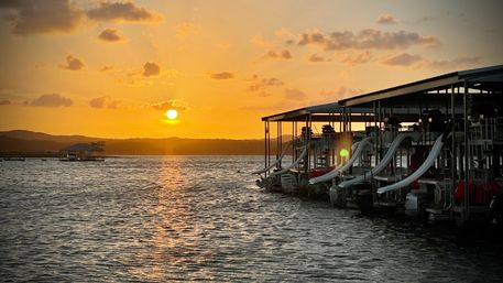 Golden sunset over a lake marina with docked boats and white water slides reflecting on rippling water.