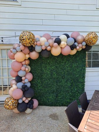 Outdoor backyard photo wall with a blush, mauve, gray, black and rose-gold balloon garland, leopard-print balloons and a green boxwood backdrop for parties