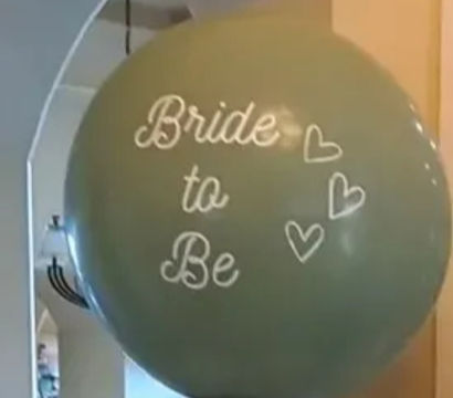 Sage-green “Bride to Be” jumbo balloon column with cream, gold and green clusters, eucalyptus garland and potted plants in an indoor entryway bridal shower display