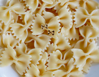 Close-up of cooked farfalle (bow-tie) pasta in a white bowl with two tiny gold bow-shaped charms on top