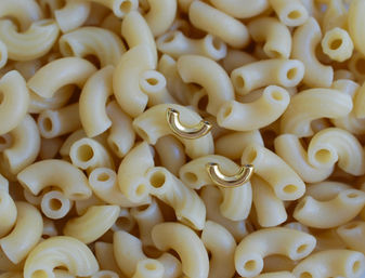 Close-up of two small gold half-hoop earrings nestled in a pile of uncooked elbow macaroni pasta