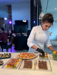 Chef in a white jacket arranging gourmet hors d'oeuvres on a white table at a modern indoor catered event — smoked salmon canapés, crostini and savory tarts.