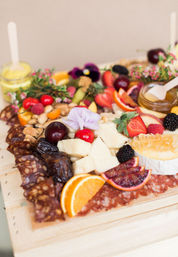 Colorful artisan charcuterie board on wood with brie and honeycomb, sliced cured meats, orange and blood orange slices, strawberries, cherries, blackberries, dates, nuts and edible flowers.