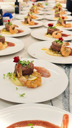 Fine-dining plated surf-and-turf dishes lined up for service: seared beef medallions and jumbo shrimp on creamy mashed potatoes, microgreens, an edible flower and red wine reduction in a restaurant kitchen.