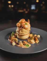 Gourmet seafood stack of golden puff pastry rounds topped with seared shrimp and mussels, drizzled with creamy seafood sauce and microgreens on a dark plate in a dim bistro setting