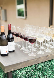 Rows of red and white wine glasses and two wine bottles on a wooden serving table, ready to serve at an outdoor reception or wine tasting