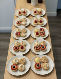 White plates lined on a wooden counter holding bite-sized fruit and lemon tarts topped with fresh berries and toasted meringue, arranged in neat rows for serving
