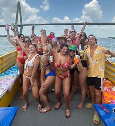 Group of friends in colorful swimwear partying on a yellow boat, holding drinks and smiling with a cable-stayed bridge and blue sky over a coastal river in the background.
