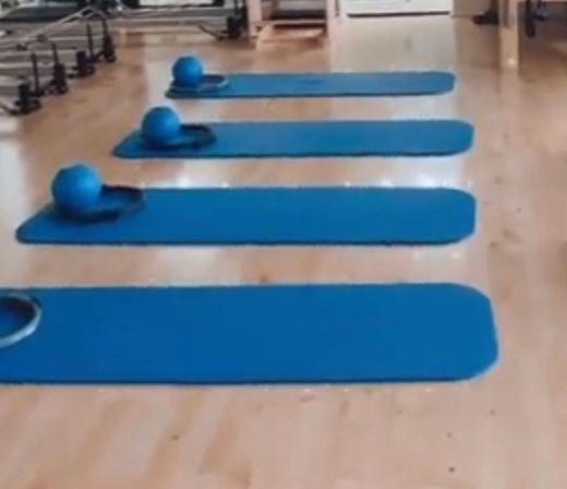 Empty fitness studio with five blue Pilates mats and matching small stability balls neatly lined on a light wood floor, ready for class.