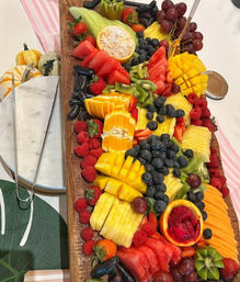 Vibrant party fruit platter on a wooden board with sliced mango, pineapple, watermelon, kiwi, blueberries, strawberries, raspberries, grapes and dragon fruit.