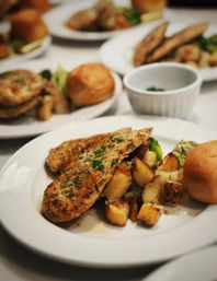 Herb-crusted grilled chicken breast with golden roasted potato cubes, parsley garnish and a warm dinner roll on a white plate — plated restaurant/banquet meal.