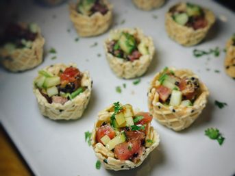 Mini sesame wonton cups filled with ahi tuna poke, diced cucumber and fresh herbs on a white plate — bite-sized appetizer