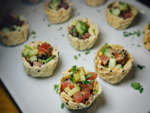 Mini sesame wonton cups filled with ahi tuna poke, diced cucumber and fresh herbs on a white plate — bite-sized appetizer