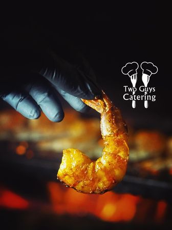 Close-up of a gloved hand holding a glazed grilled shrimp above glowing barbecue coals, golden sauce glistening with smoky orange bokeh in the background.