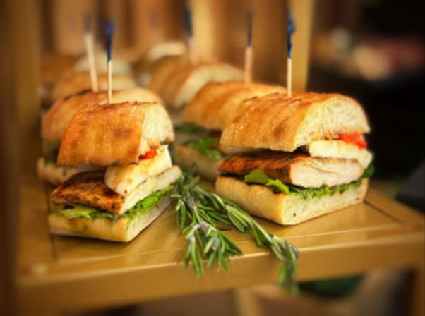 Mini grilled chicken ciabatta sliders with roasted red pepper and lettuce, skewered with toothpicks and garnished with fresh rosemary on a serving tray