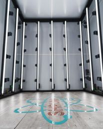 Sleek empty LED-lit photo studio booth with vertical white light bars on gray walls and a wood-look floor marked by a turquoise graphic logo — modern indoor product and portrait lightbox.