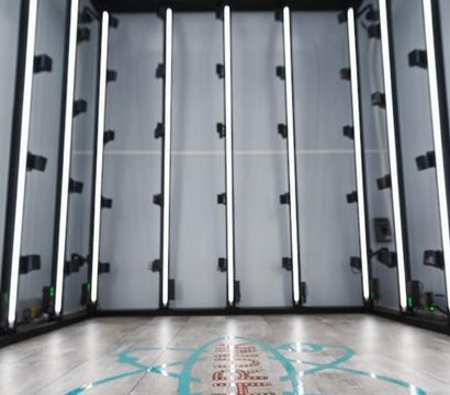 Sleek empty LED-lit photo studio booth with vertical white light bars on gray walls and a wood-look floor marked by a turquoise graphic logo — modern indoor product and portrait lightbox.
