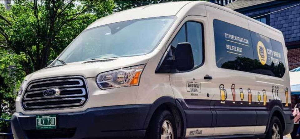 White passenger van with brewery-themed beer glass graphics and dark windows parked on a tree-lined urban street