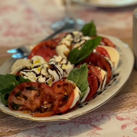Classic Italian Caprese salad with sliced heirloom tomatoes, fresh mozzarella, basil leaves and balsamic glaze on a white platter