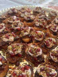 Platter of bite-sized toasted crostini topped with creamy yogurt, pomegranate arils, chopped pistachios and a sweet glaze — colorful Mediterranean-style appetizers.