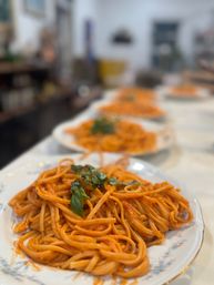 Close-up of plated spaghetti pasta in rich tomato sauce topped with fresh basil, multiple servings lined up on a white table in a cozy Italian-style dining setting
