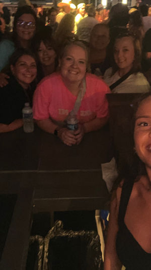 Smiling woman taking a selfie with a group of friends at a crowded indoor bar, people gathered around the bar counter under warm dim lights for a lively nightlife scene.