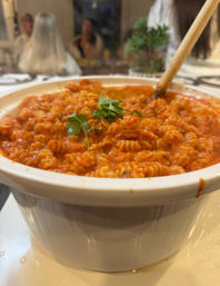 Close-up of steaming rotini pasta in rich tomato sauce, garnished with parsley in a white baking dish on a cozy dinner table