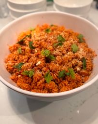 Hearty tomato rotini pasta in red sauce, sprinkled with grated Parmesan and fresh parsley, served in a white bowl on a kitchen countertop