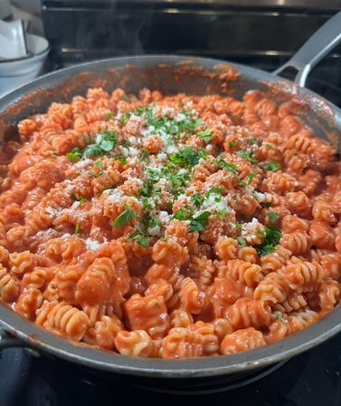 Steaming rotini pasta in a creamy tomato sauce, sprinkled with grated Parmesan and chopped parsley in a skillet on the stovetop