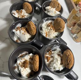 Black ceramic mugs on a marble countertop filled with vanilla ice cream and whipped cream, sprinkled with cookie crumbs and each garnished with a gingersnap cookie, ready-to-serve party dessert.