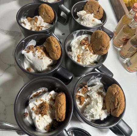 Black ceramic mugs on a marble countertop filled with vanilla ice cream and whipped cream, sprinkled with cookie crumbs and each garnished with a gingersnap cookie, ready-to-serve party dessert.