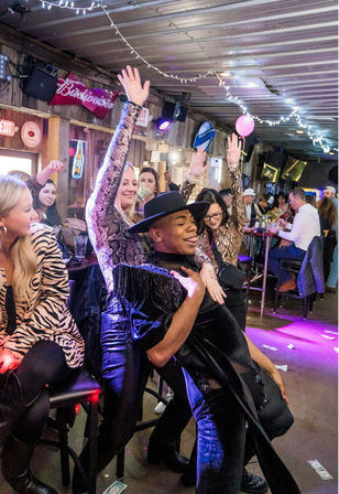 Lively indoor bar nightlife scene with people dancing and cheering under string lights, a person in a hat striking a dramatic pose and dollar bills scattered on the floor.