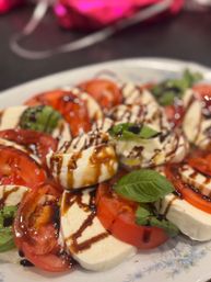 Close-up Caprese salad with sliced ripe tomatoes, fresh mozzarella rounds, basil leaves and a balsamic glaze drizzle on a white plate
