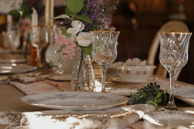 Elegant tablescape with gold-rimmed crystal wine glasses, fine china plates, gold flatware and a textured glass vase of white and pink flowers and greenery