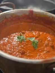 Close-up of simmering homemade tomato meat sauce bubbling in a stainless pot, topped with fresh basil leaves — rich Italian-style marinara in a kitchen.
