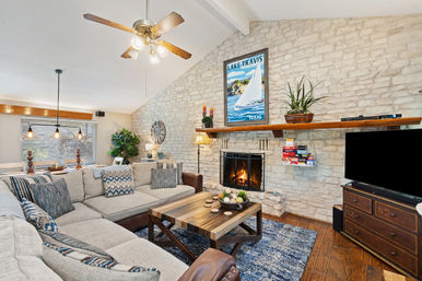 Cozy Texas living room with large gray sectional, wooden coffee table, stone accent wall and lit fireplace beneath a 'Lake Travis, Texas' sailboat poster
