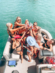 Group of friends in bikinis toasting canned drinks on a pontoon boat over turquoise water on a sunny summer day