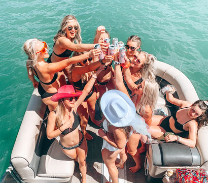 Group of friends in bikinis toasting canned drinks on a pontoon boat over turquoise water on a sunny summer day
