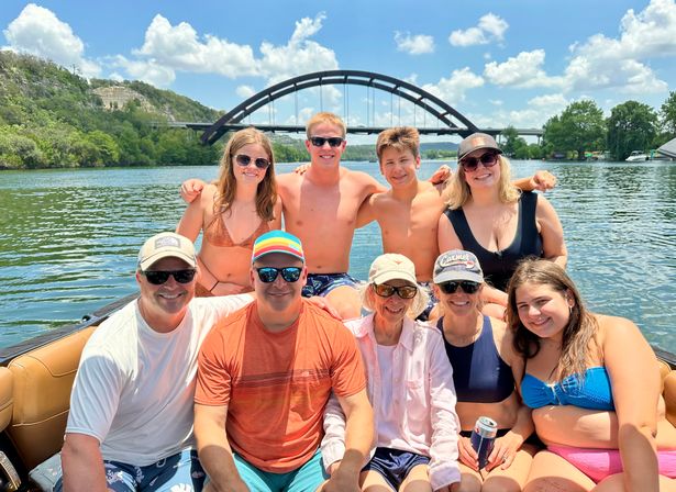 Smiling group of friends and family on a boat in swimsuits, posing on a sunny summer day with the arched Pennybacker (360) Bridge over Lady Bird Lake in Austin, Texas in the background.