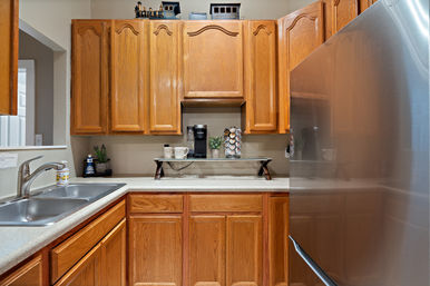 Bright residential kitchen with oak cabinets, stainless steel refrigerator, double sink, and a countertop coffee station with a single-serve coffee maker and K-cup carousel.