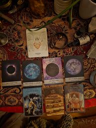 Boho-style oracle and tarot card spread on a patterned tapestry featuring an angel Sophia wisdom card, moon-phase and full moon cards, Merlin, Love and King cards, surrounded by crystals, dropper bottles, a brass cup and ritual items on a cozy tabletop altar.