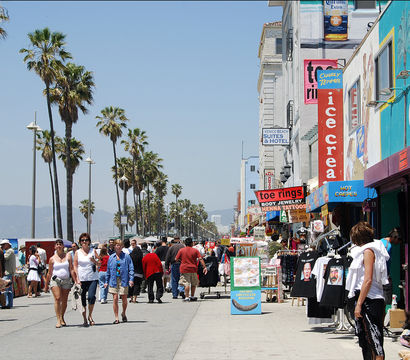 Venice Beach boardwalk in Los Angeles - sunny, palm-lined promenade with colorful beachside shops, street vendors and crowds walking and biking.