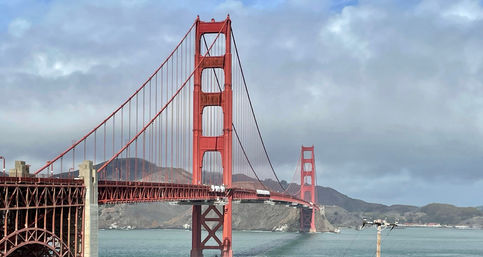 Golden Gate Bridge in San Francisco spanning blue-green bay under a cloudy sky, red suspension towers and cables with the Marin Headlands in the background