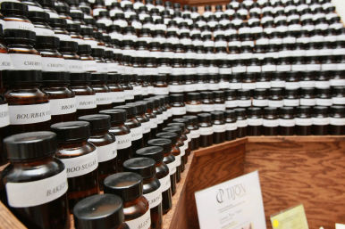 Tiered wooden display filled with rows of small amber glass bottles with white labels and black caps — apothecary-style flavor and fragrance samples.