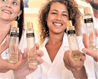 Close-up of a smiling group holding tall glass perfume bottles with gold caps and custom labels during a boutique fragrance tasting